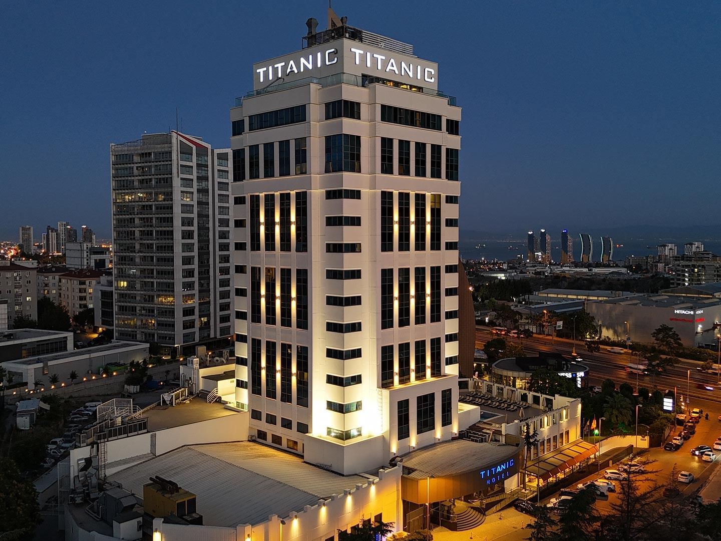 Nighttime aerial view of the illuminated Titanic Business Kartal Hotel in a city skyline.
