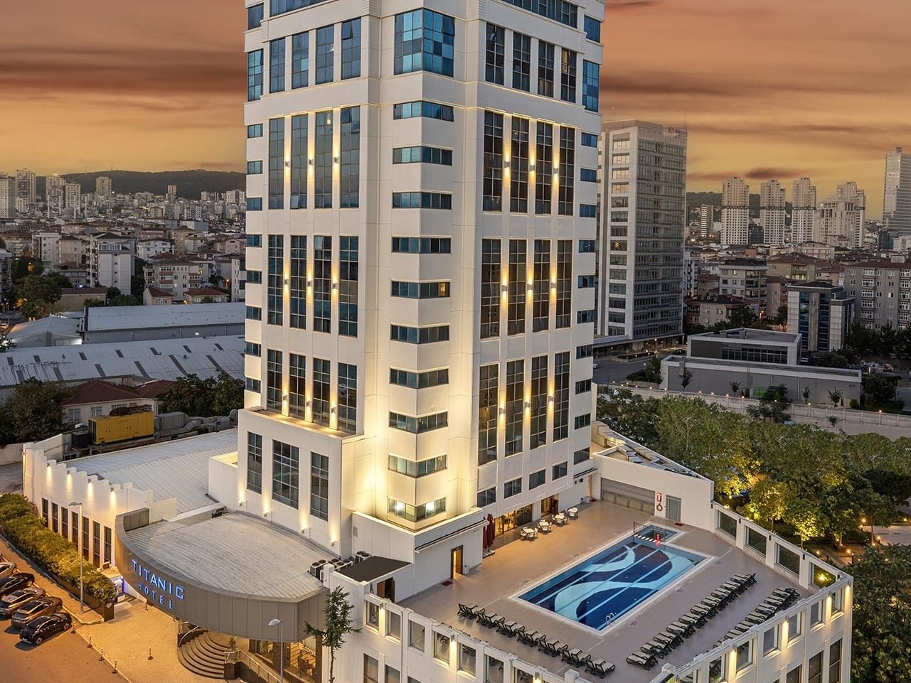 Elevated view of Titanic Hotel with rooftop pool, surrounded by urban landscape and parked cars.