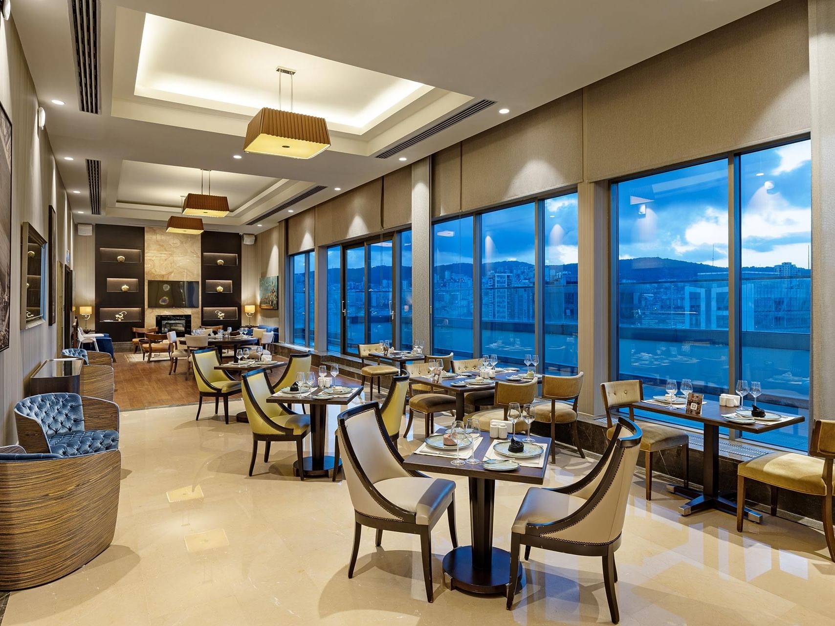 Elegant dining area with large windows, modern furniture, a view of cityscape under a clear sky in Titanic Business Kartal.