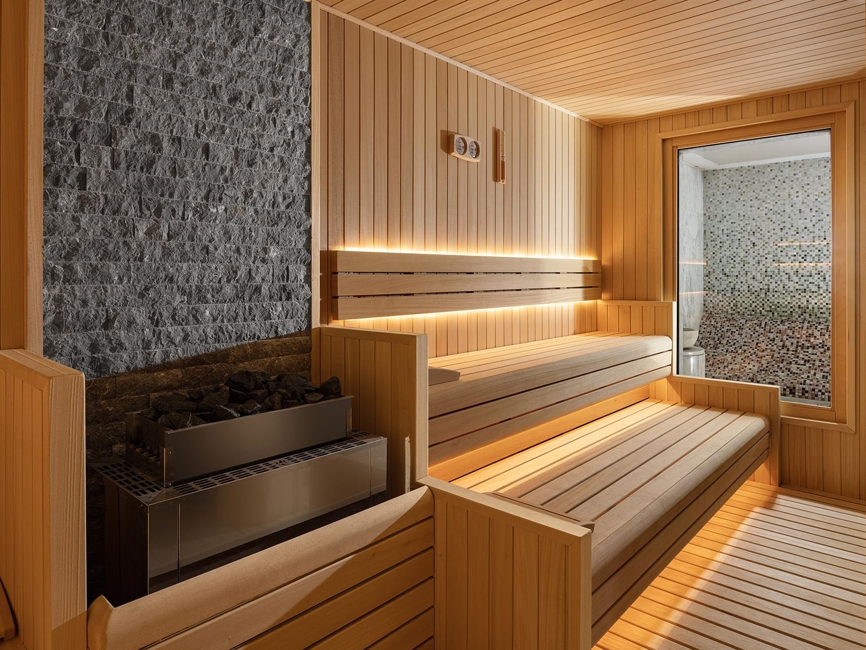 Wooden sauna with benches, a gray stone wall in Befine Spa at Titanic Business Kartal