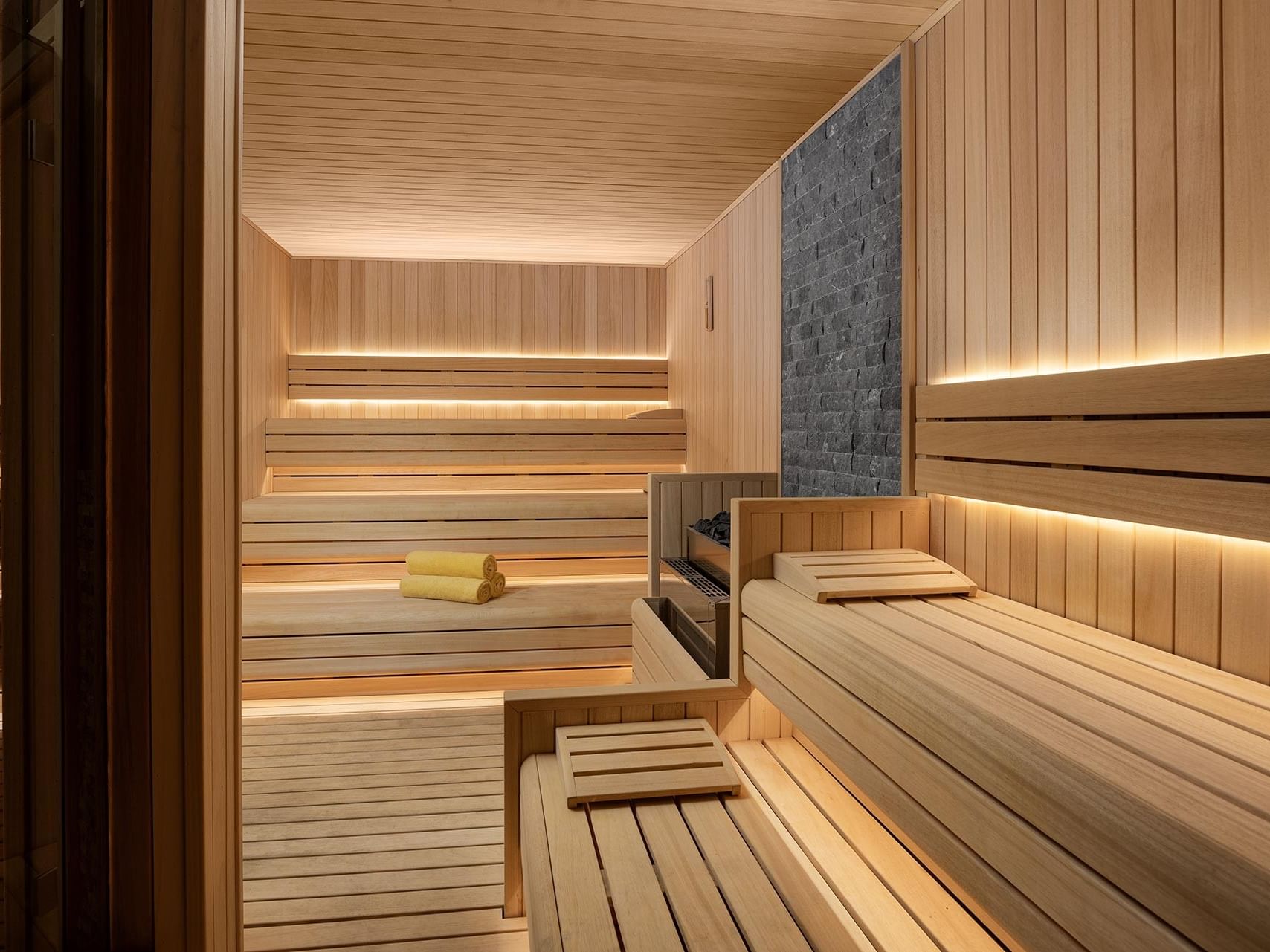 Wooden sauna with built-in benches, a stone wall, & ambient lighting in Befine Spa at Titanic Business Kartal