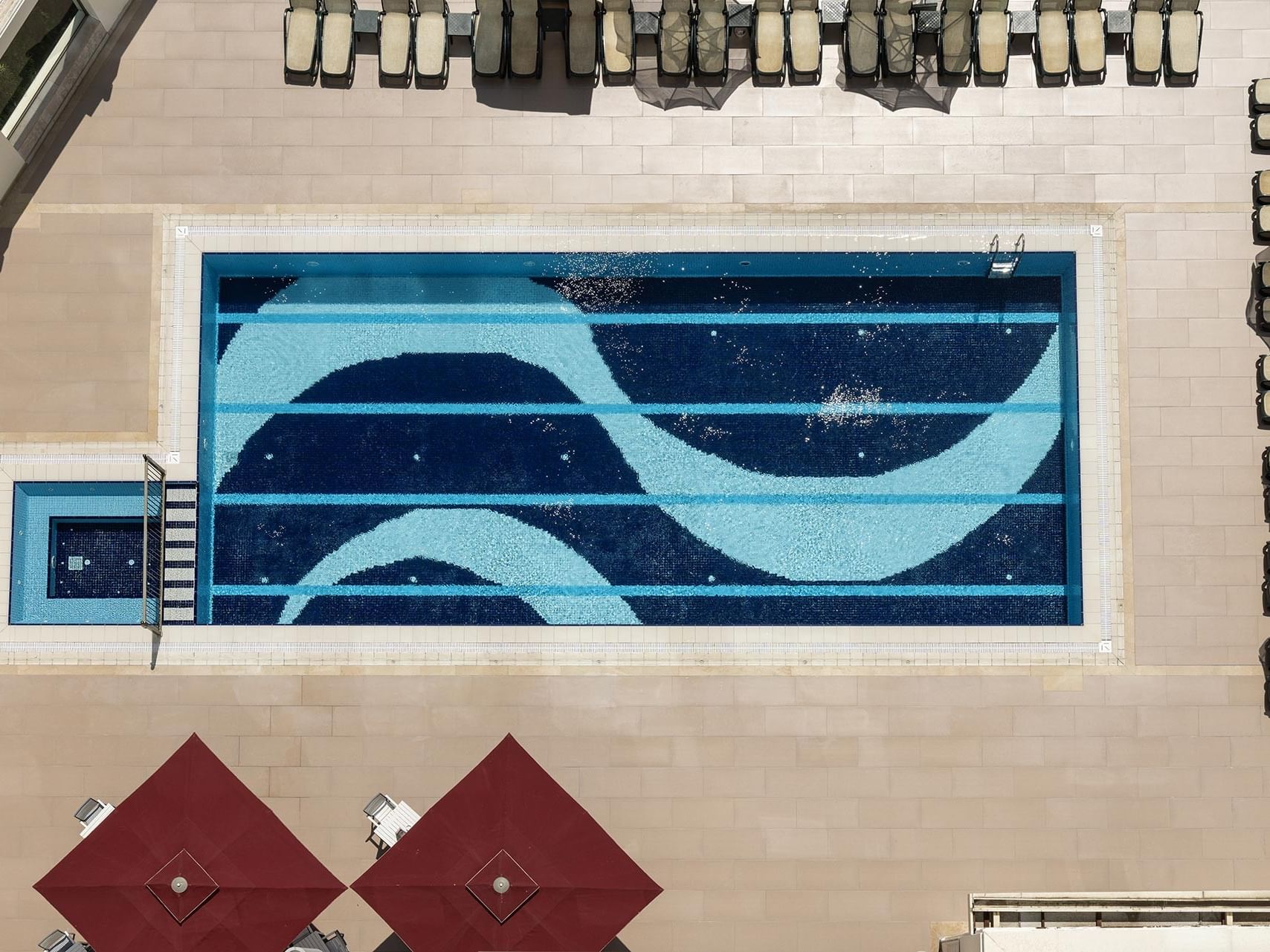 An aerial view of a pool with a blue wave design, surrounded by lounge chairs in Befine Spa at Titanic Business Kartal