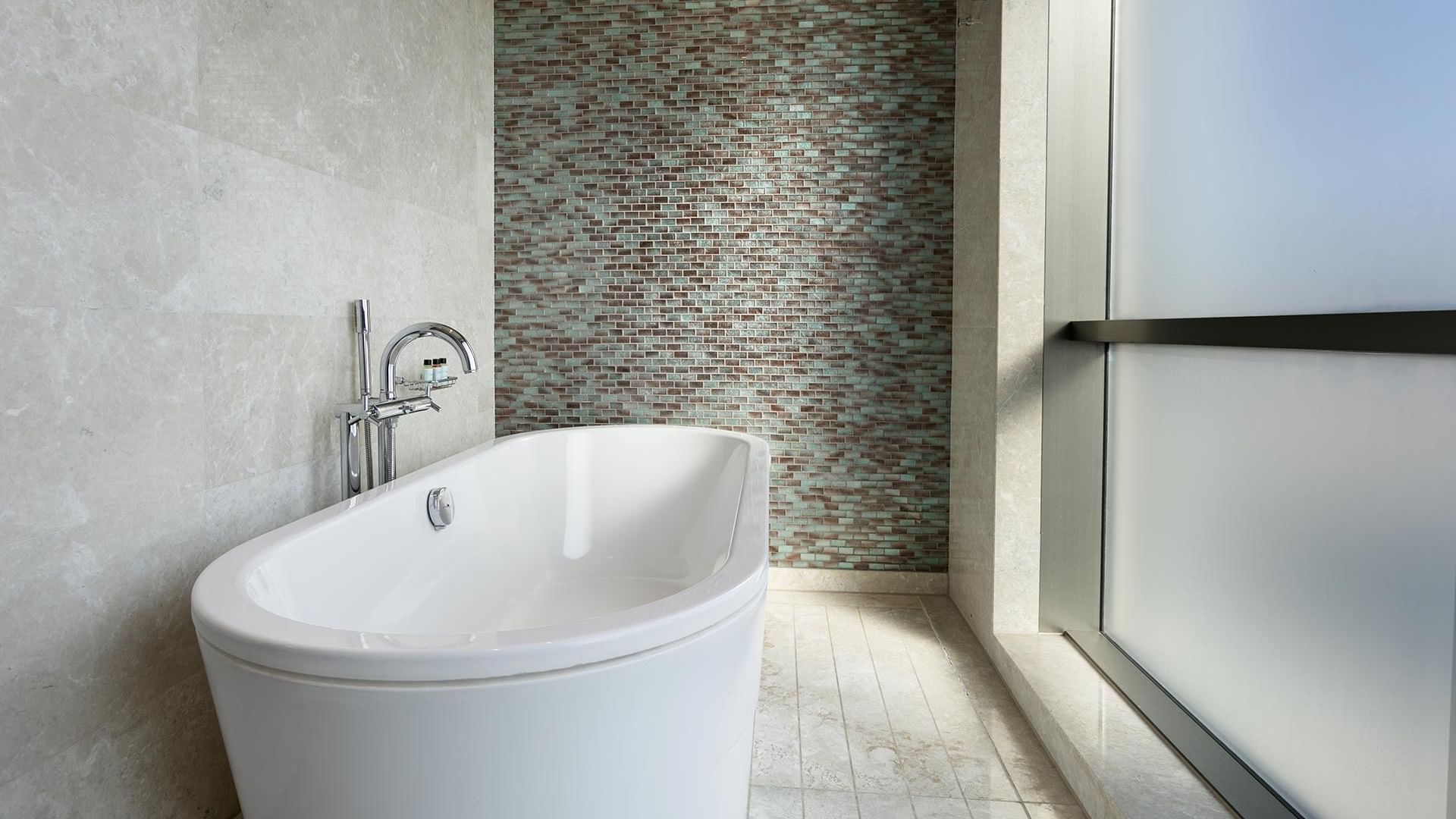 White bathtub with a modern faucet and tiled wall in the Deluxe Room at Titanic Business Kartal in Istanbul.