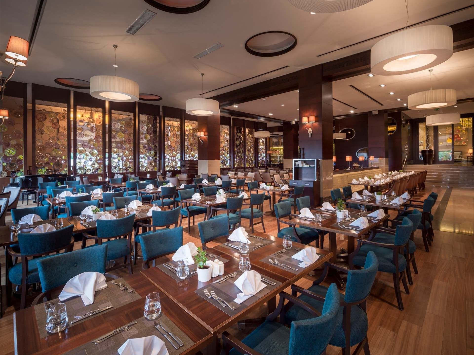 An elegant dining room with blue chairs and wooden tables set for dinner at Titanic Business Kartal.
