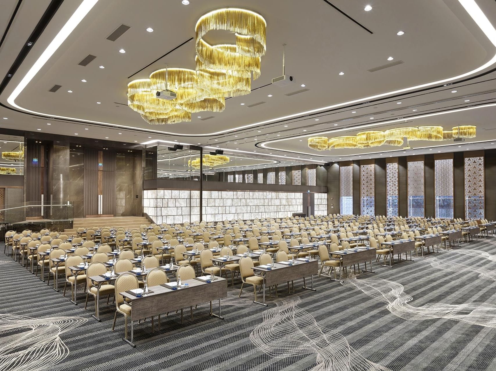 A large conference hall with rows of chairs and tables under gold chandeliers at Titanic Business Kartal.