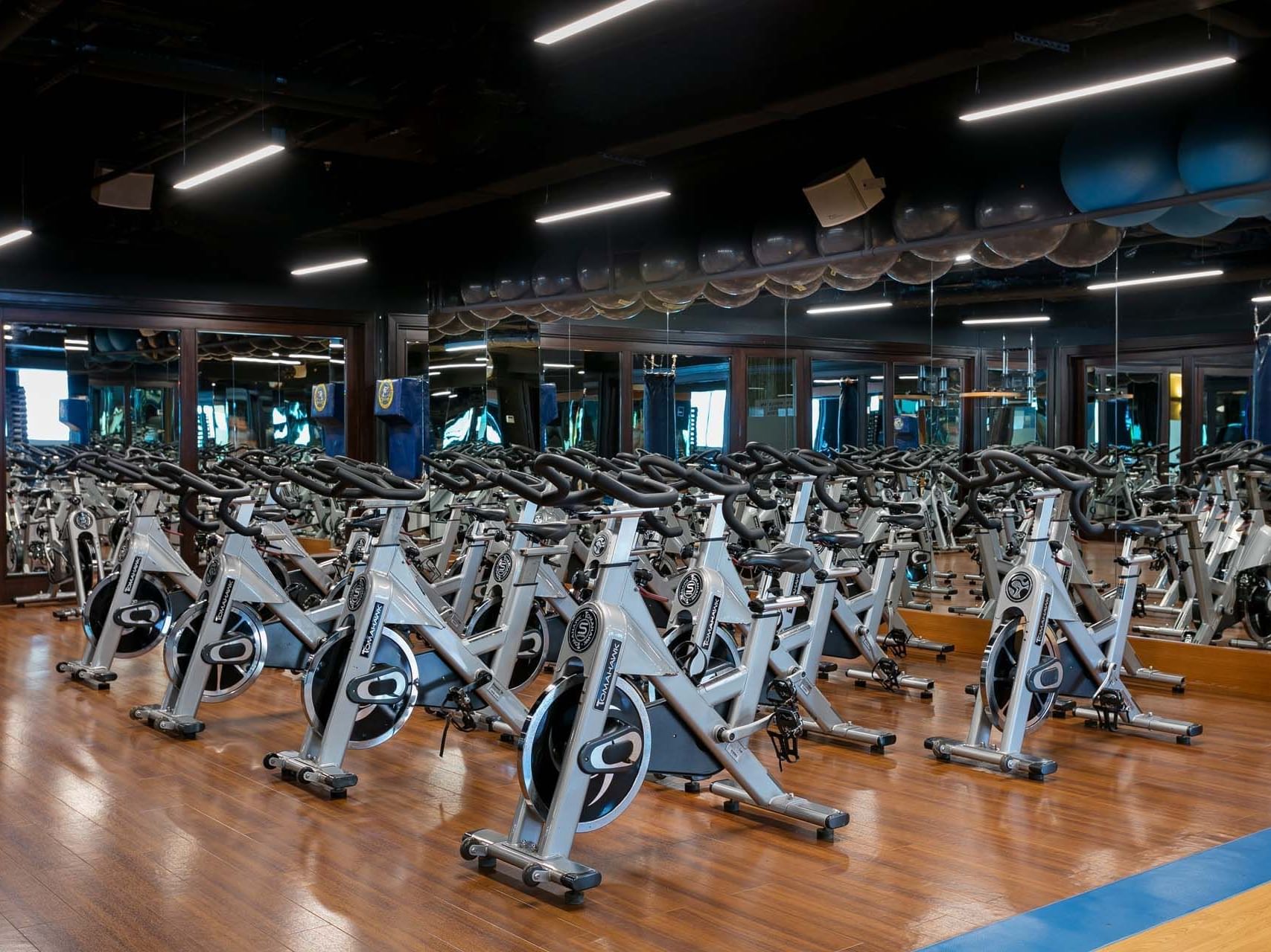 Many exercise bikes in a gym with hardwood floors and ceiling lights.