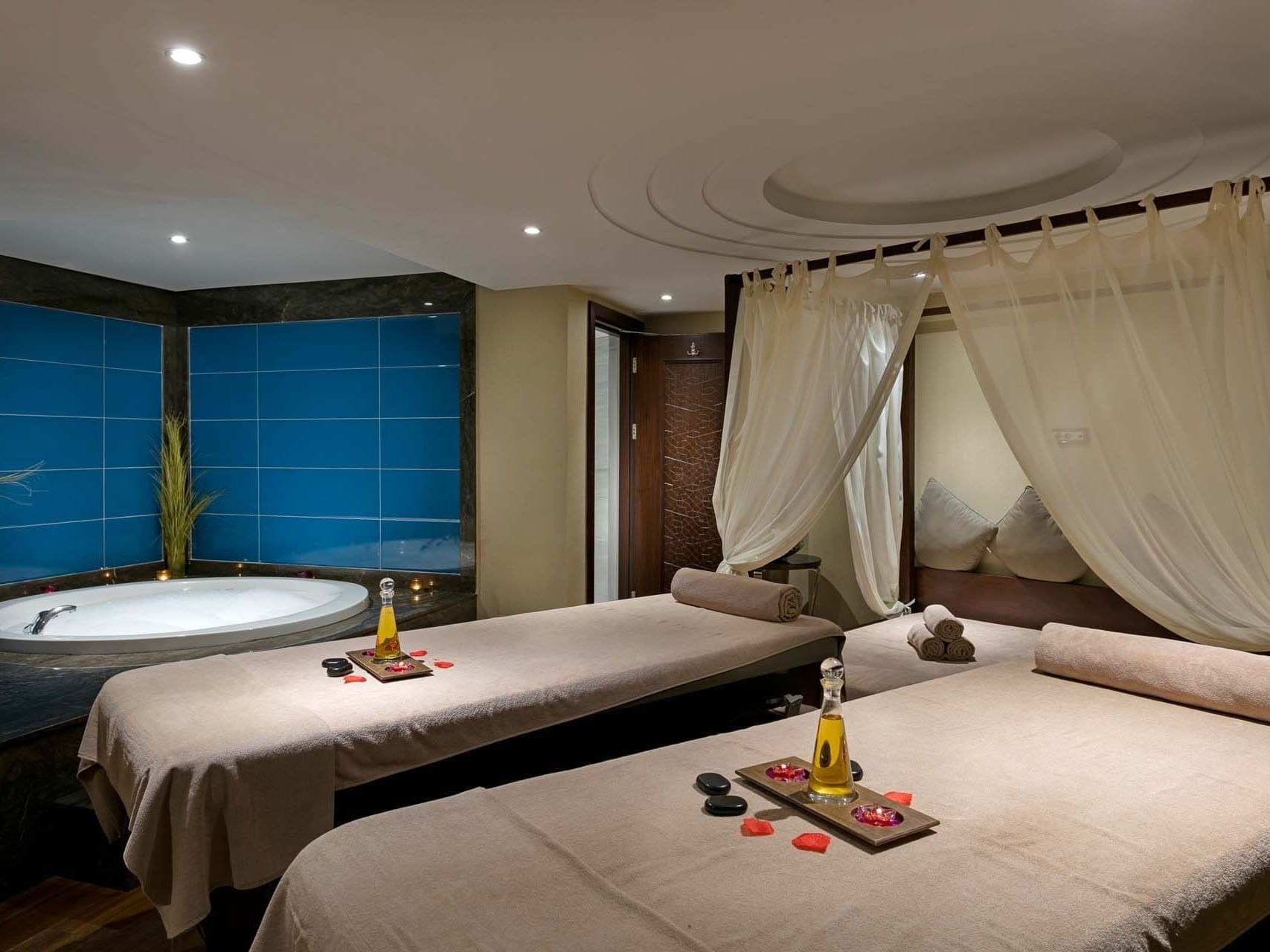 Two massage beds in a spa room with blue tiles and a bathtub at Titanic Business Kartal.