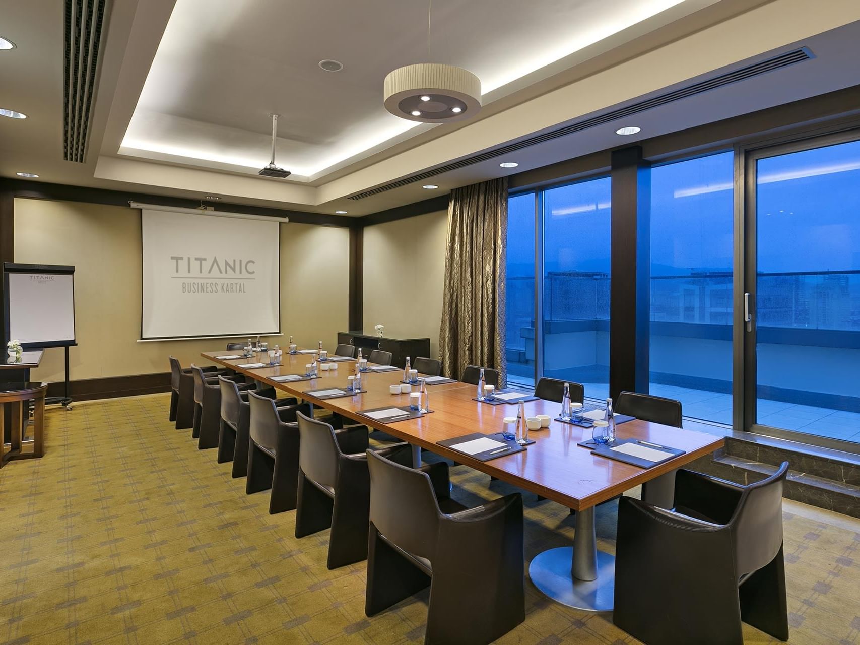 A long table with chairs and a large screen in Compass Meeting Room at Titanic Business Kartal