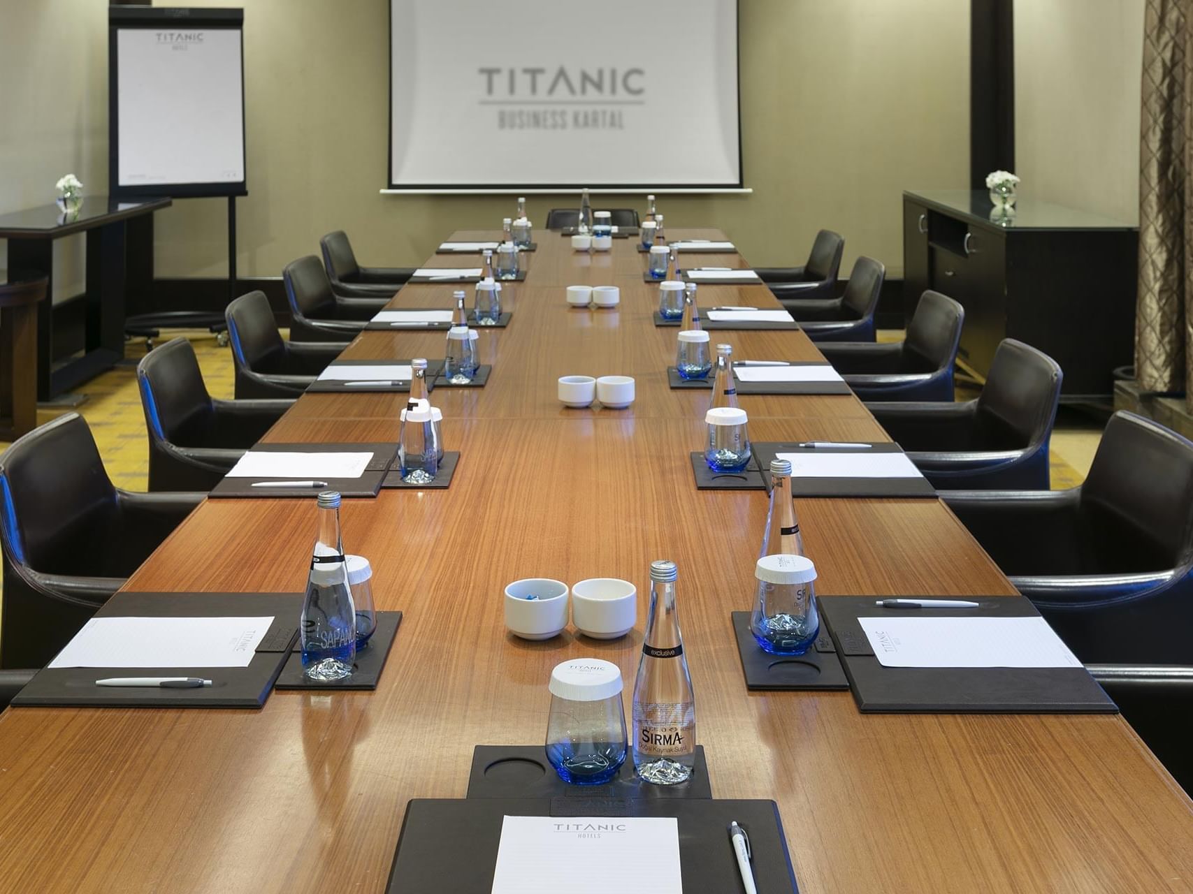 A long meeting table with chairs and a large screen in Compass Meeting Room at Titanic Business Kartal