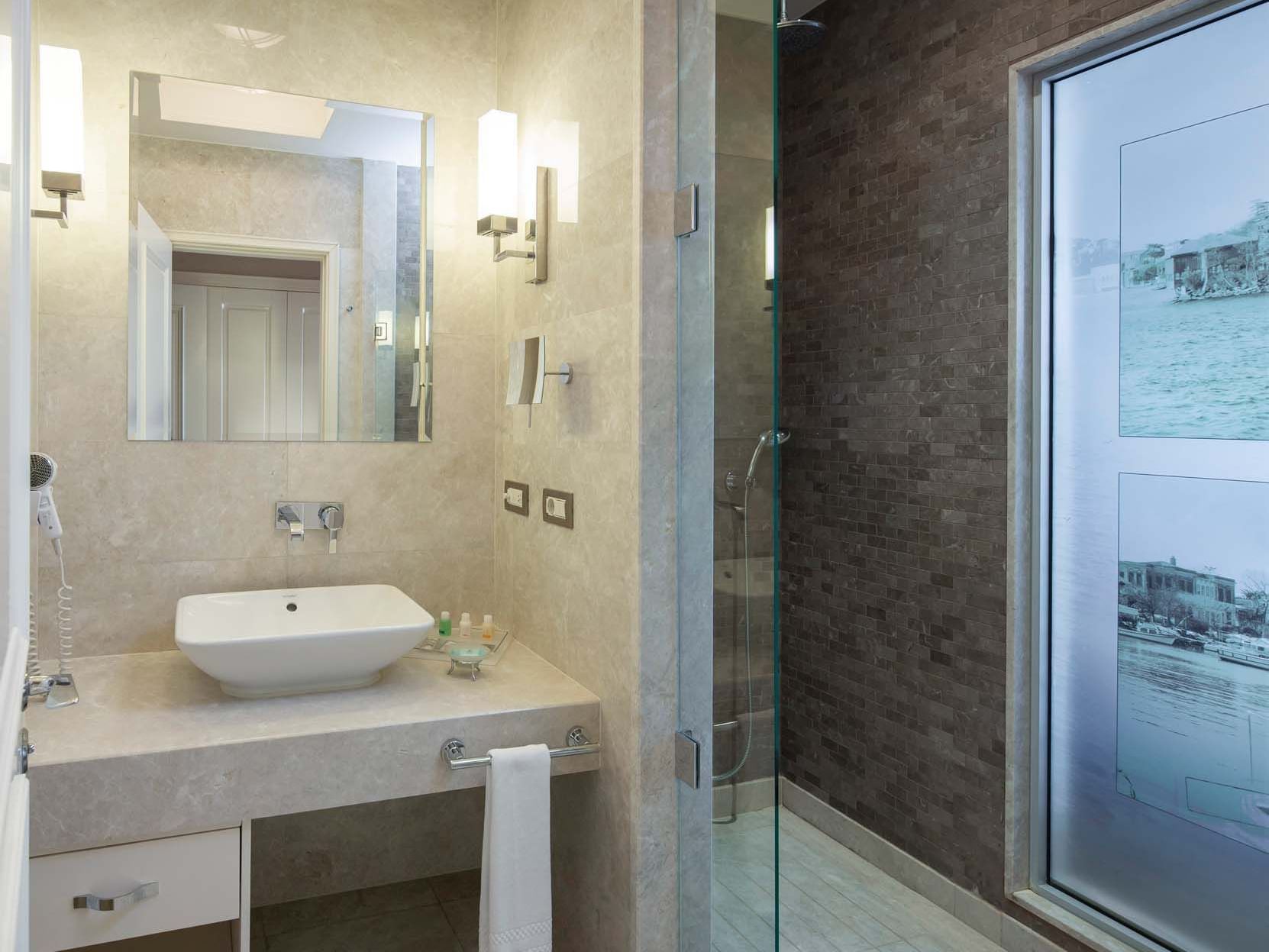 Modern hotel bathroom with a sink, mirror, and glass shower enclosure at Titanic Business Kartal.