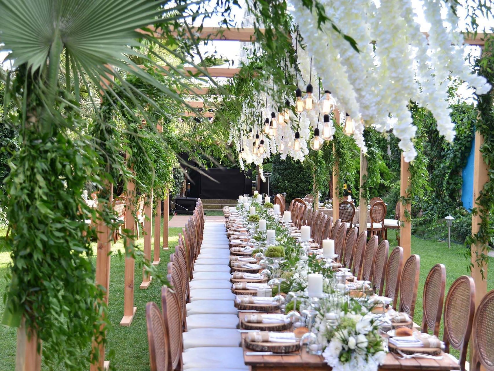 A long table set up for an event with white flowers and candles in an outdoor garden.