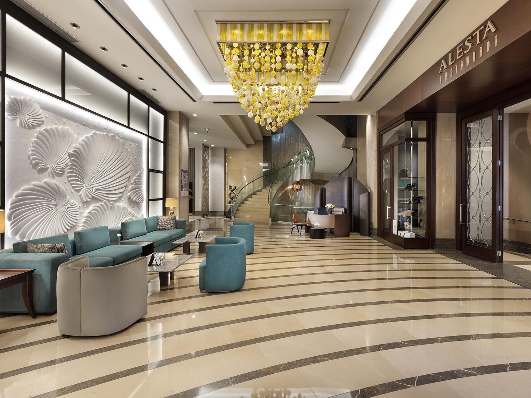 Elegant lobby with modern furniture, spiral staircase, and chandelier at Titanic Business Kartal.