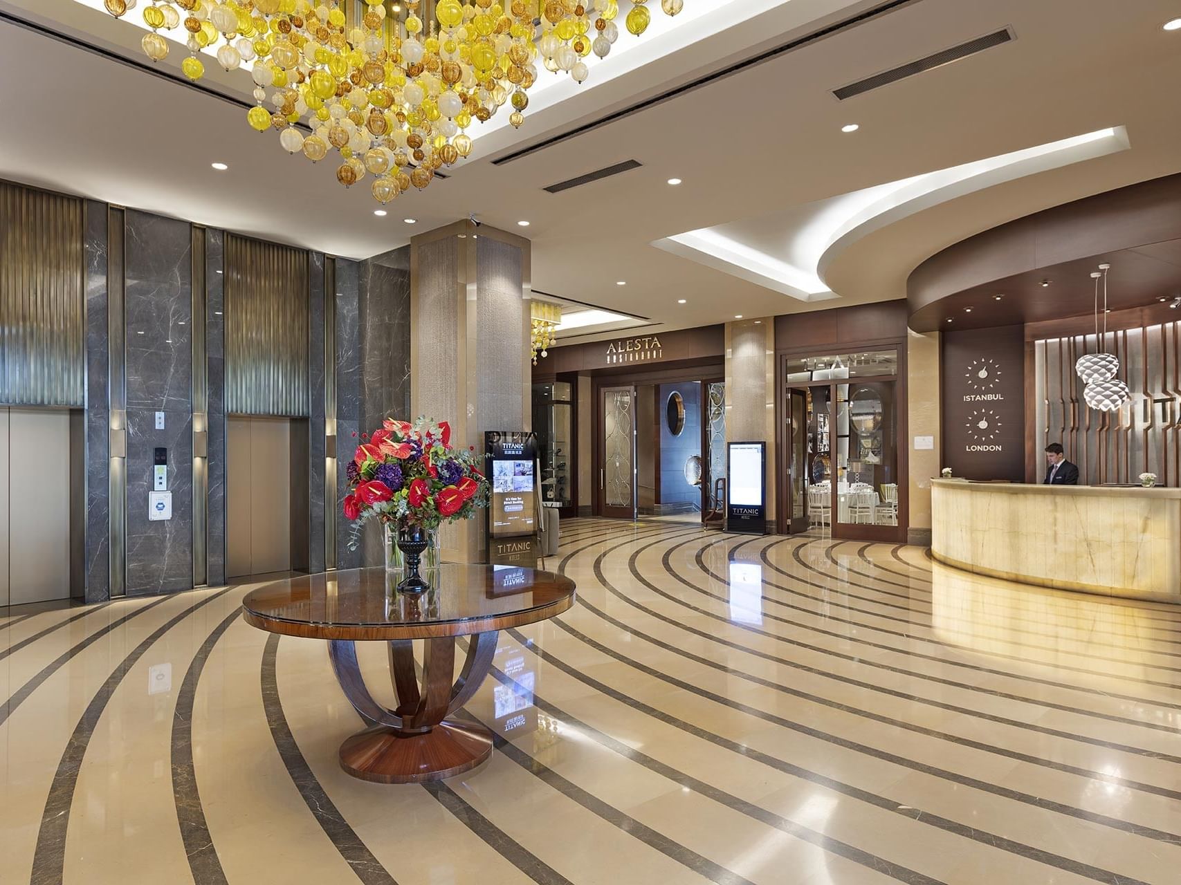 Reception area with a round table, large chandelier, and floral arrangement at Titanic Business Kartal.